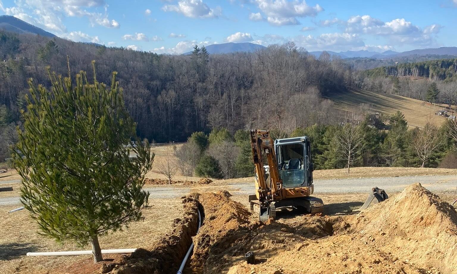 An excavator working a fresh-dug site with the Blue Ridge Mountains and a blue sky behind it
